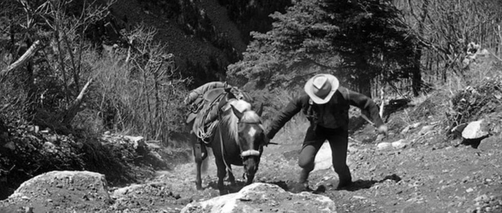 Kirk Douglas as Jack Burns, climbing up a mountain with his horse
